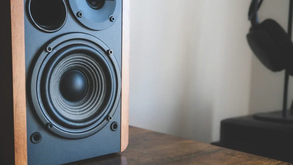 Speaker using alnico magnet placed on a wooden desk, with a headphone in the background.